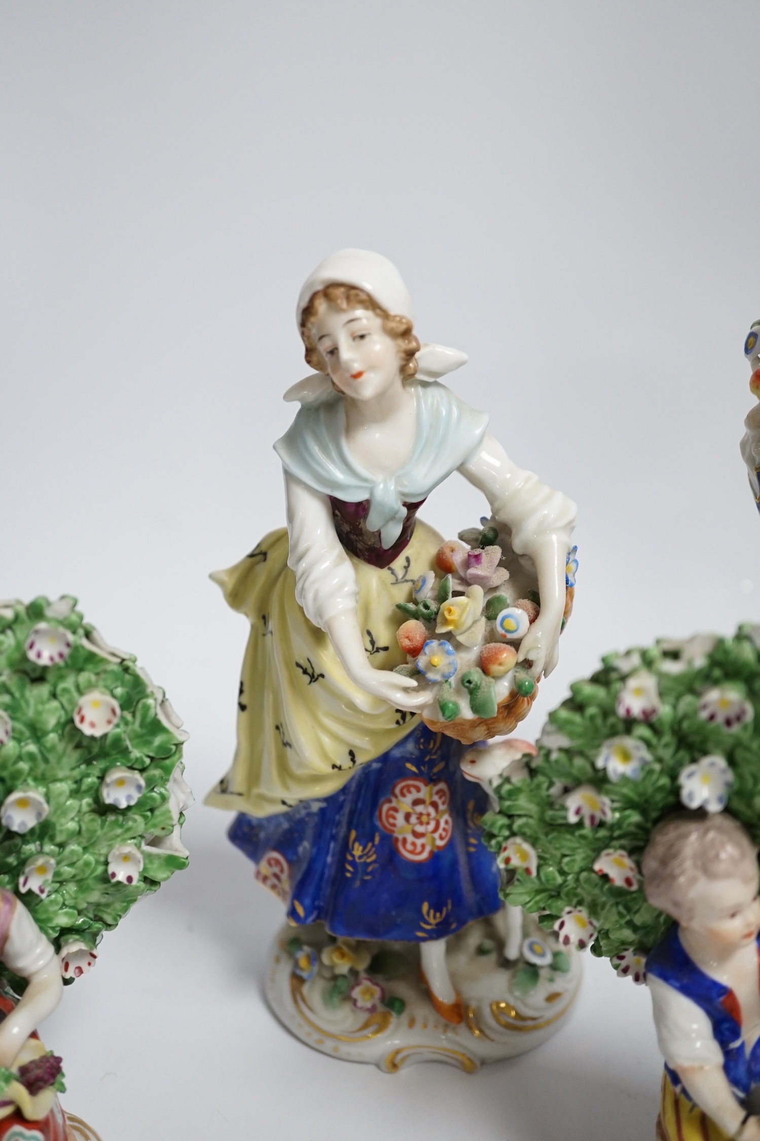A pair of Derby style porcelain small bocage figures, a boy and girl seated with grape filled hats, height 14cm, three porcelain lambs and another figure
